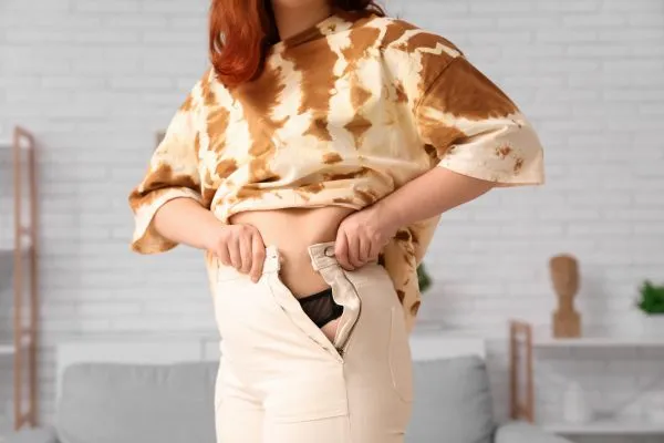 Image of woman trying to do her trousers up after pregnancy weight gain Southampton